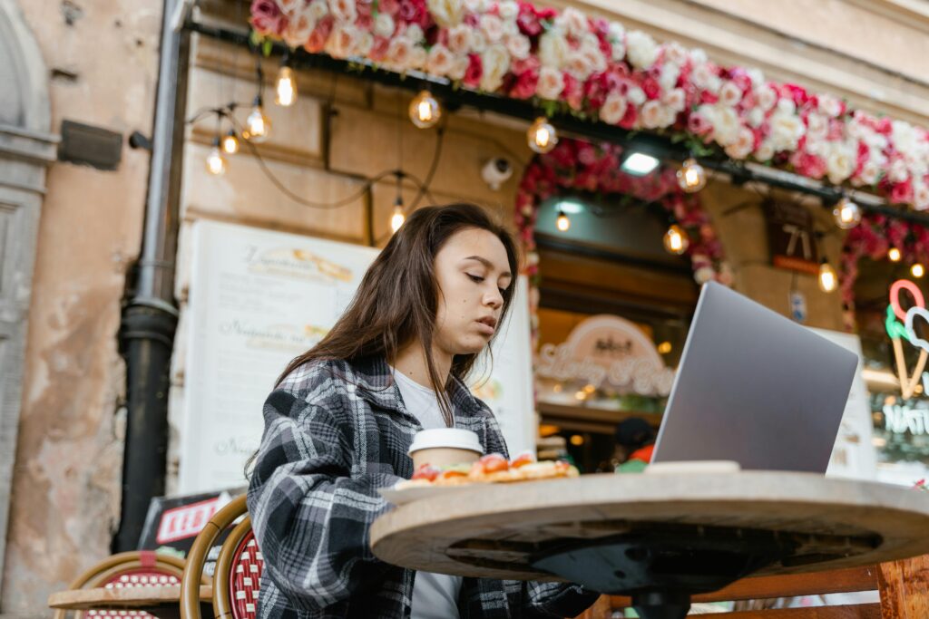 Young woman working on laptop at a café with floral decorations.